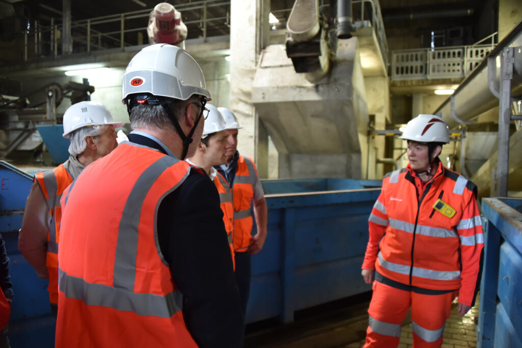 Visite d'une installation industrielle par des professionnels en gilets orange et casques de sécurité.