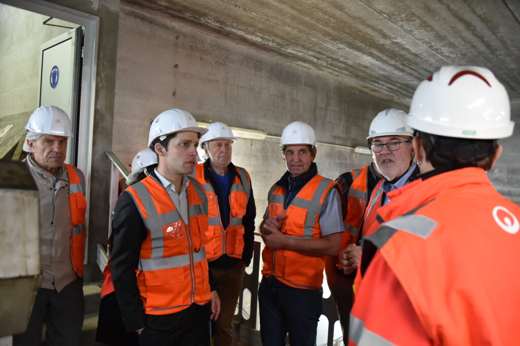 Visite d'un chantier souterrain par des ingénieurs en gilets orange et casques de sécurité blancs.