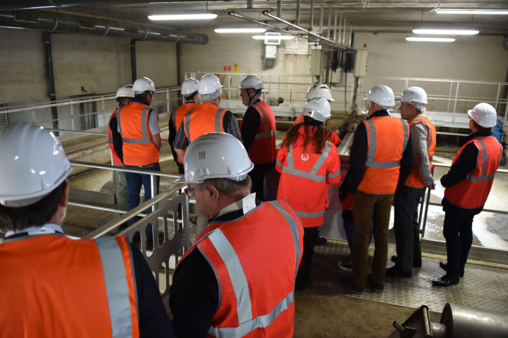 Groupe en visite industrielle avec casques et gilets de sécurité, explorant une installation de traitement des eaux.