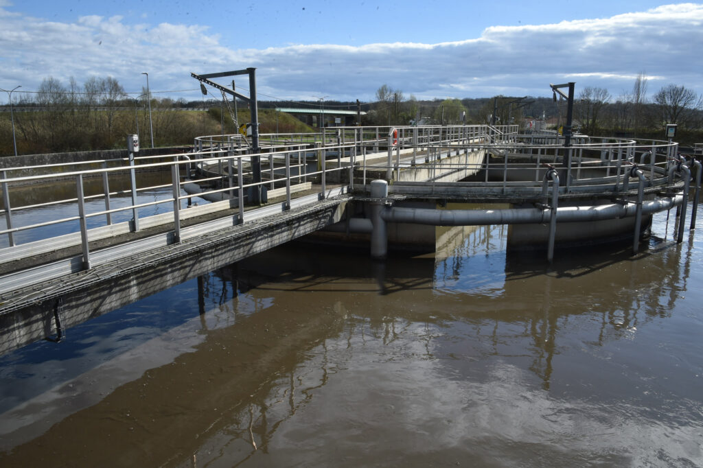 Station de traitement des eaux usées sous un ciel nuageux, ponts métalliques au-dessus de la surface de l'eau.