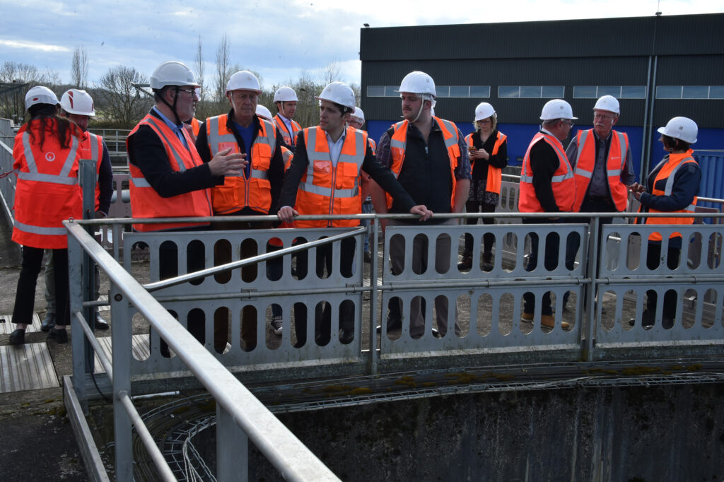 Groupe de personnes portant des casques et des gilets de sécurité visitant un site industriel extérieur.