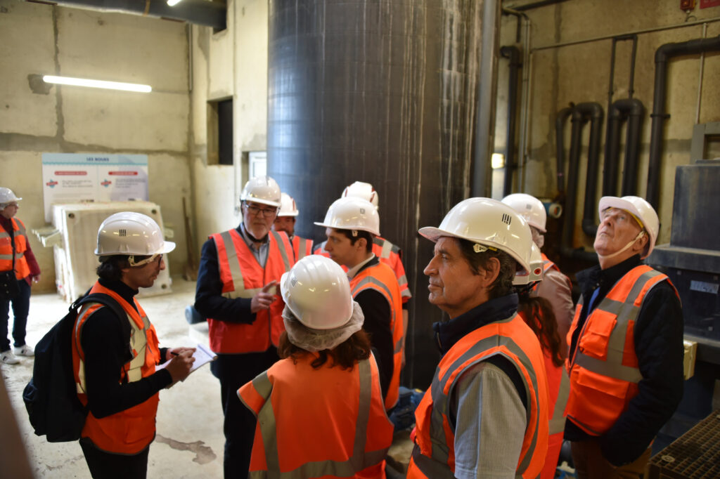 Groupe de personnes en gilet orange et casque de sécurité lors d'une visite d'un chantier industriel.