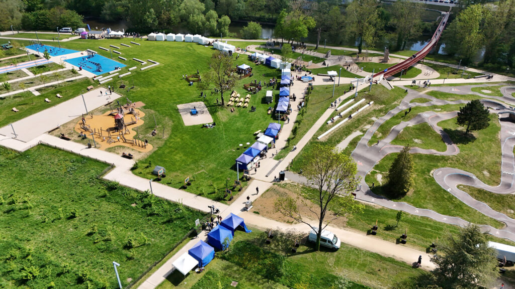 Vue aérienne d'un parc animé avec installations de loisirs, tentes blanches et bleues, et visiteurs se promenant.