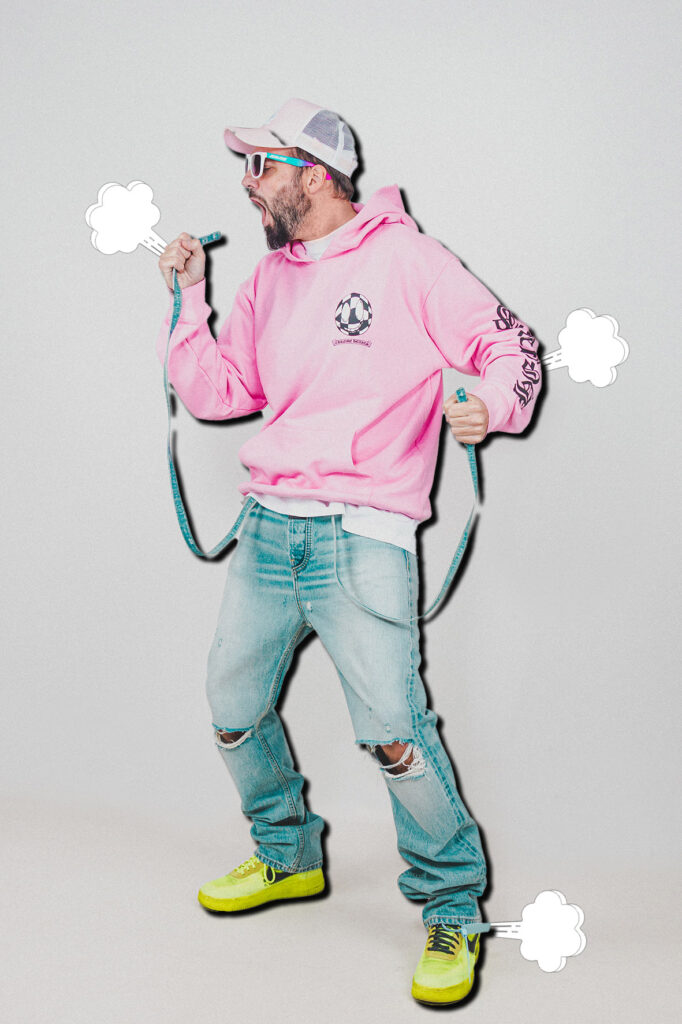 Homme en sweat rose, jeans déchiré, baskets jaunes, criant avec un mètre ruban, fond gris, style décontracté et vibrant.