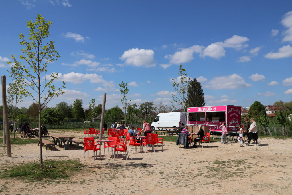 Food truck rose Chez Valentin avec chaises rouges, sous un ciel dégagé, entouré de clients en extérieur.