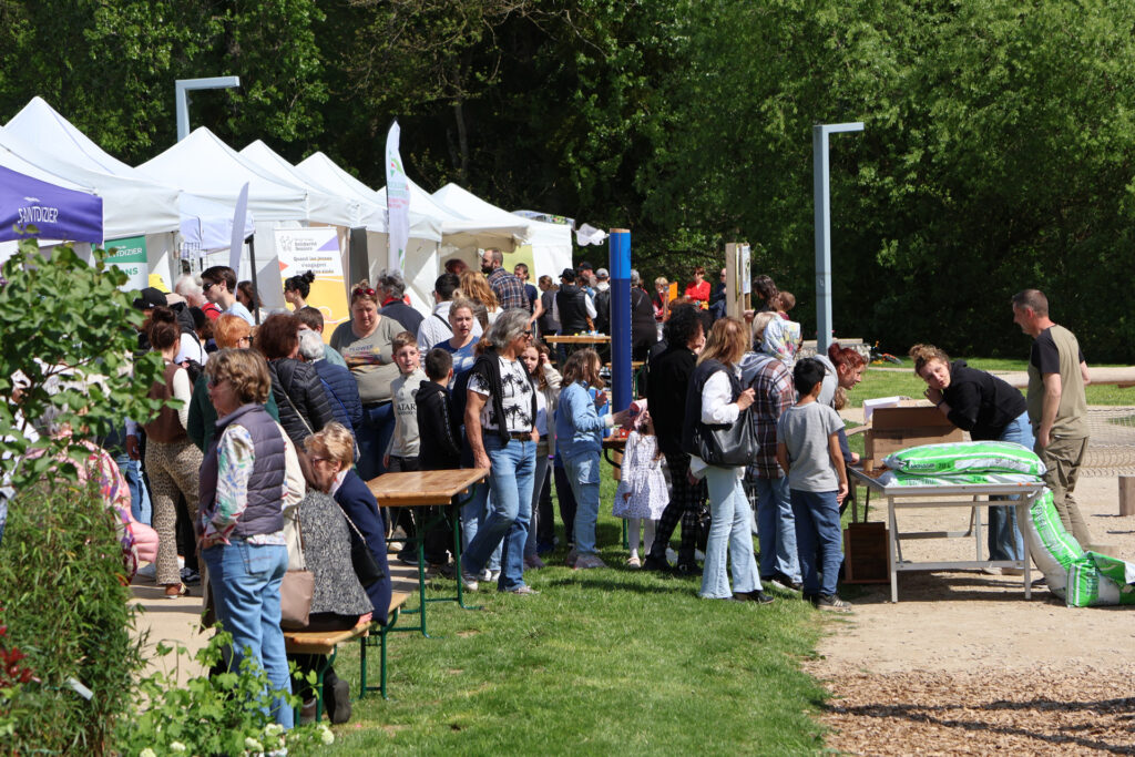 Foule rassemblée à une foire en plein air avec des stands, des activités et des discussions sous des tentes blanches.