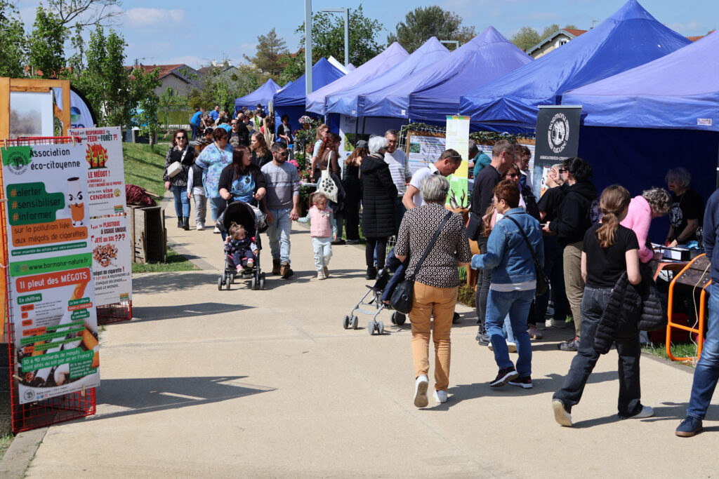 Foule se promenant dans un marché éco-citoyen avec stands d'information et sensibilisation environnementale sous tentes bleues.