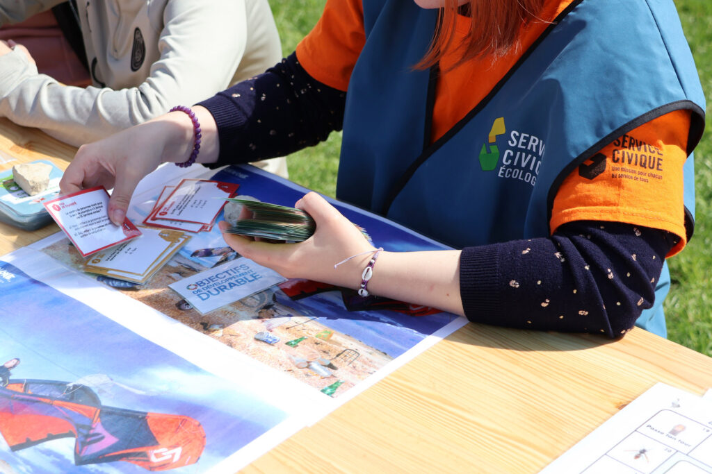 Personne en mission de Service Civique utilisant des cartes pour sensibiliser au développement durable lors d'un atelier extérieur.